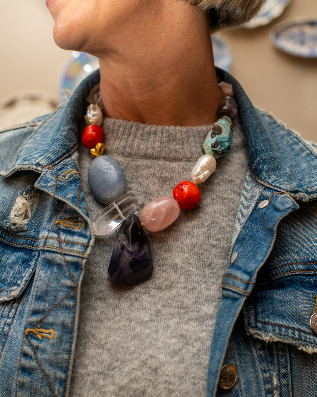 Colourful pearl and oversized gemstone statement necklace styled over a grey knit and denim jacket