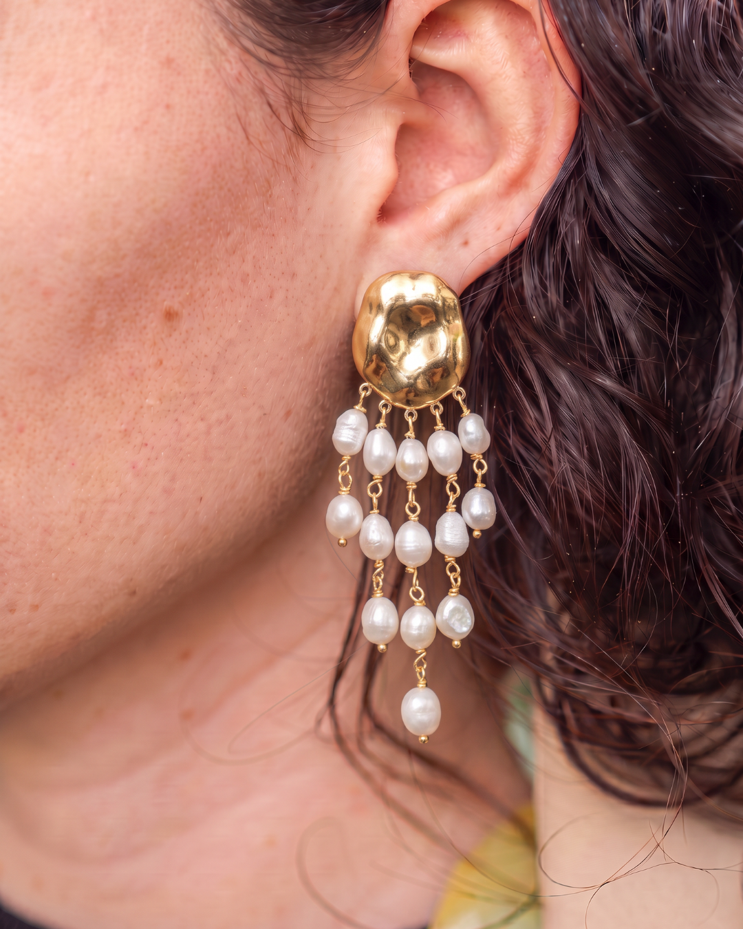 Gold-tone drop earring with cascading white beads worn on the ear