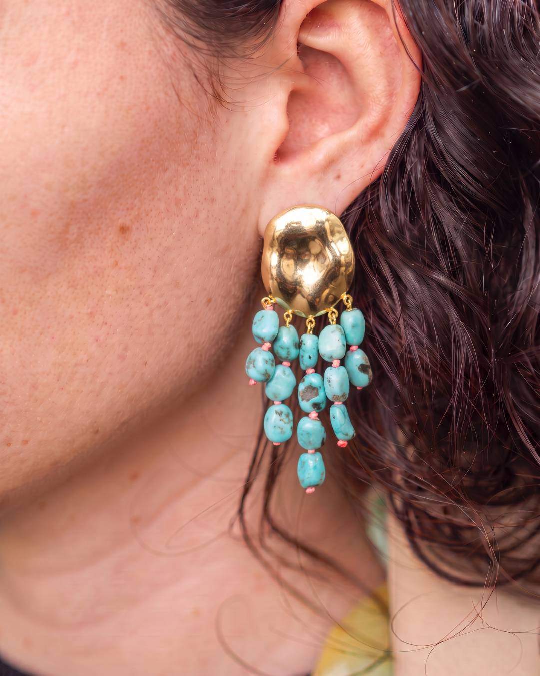 Gold-tone drop earring with cascading blue-green gemstones worn on the ear