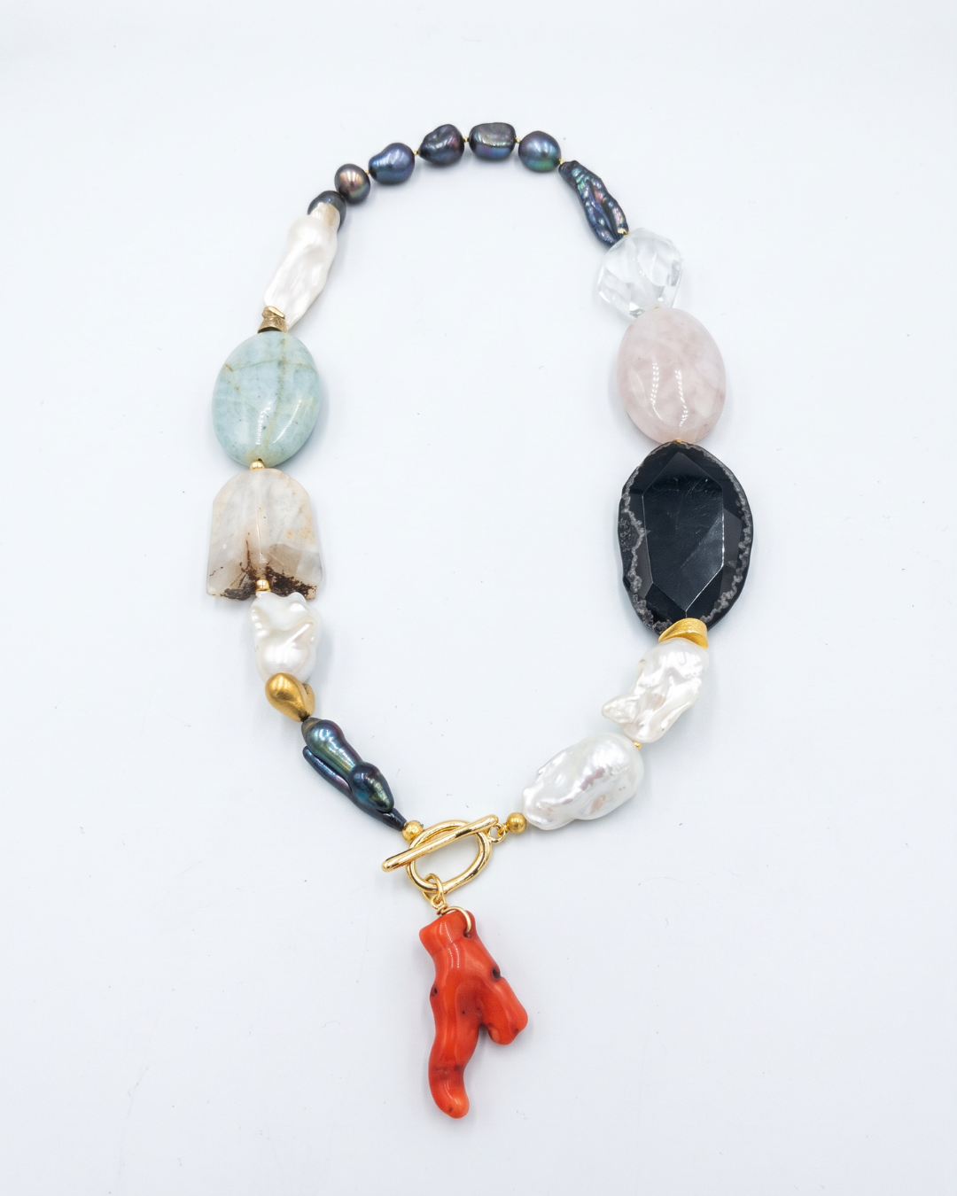 Multicolour gemstone and freshwater pearl statement necklace with red pendant on a white background